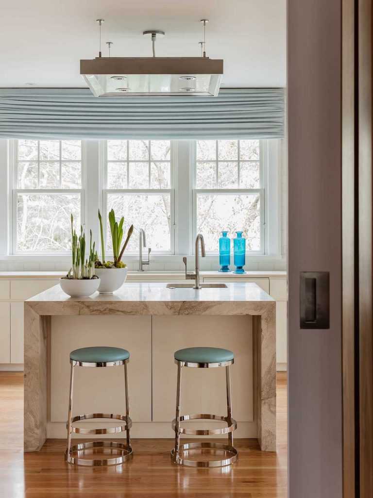 The kitchen island is wrapped in stone and features a prep sink and area as well as bar stools for casual dining. A custom light fixture above provides both general and task lighting.