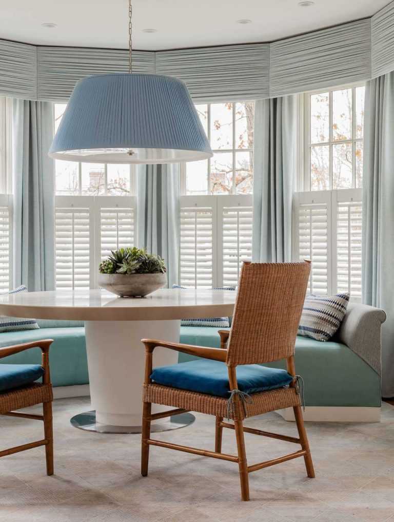 The breakfast nook is inviting with a custom banquette and center pedestal dining table that allows for seating flexibility. Window treatments encircling the nook let in natural light and also offer privacy.