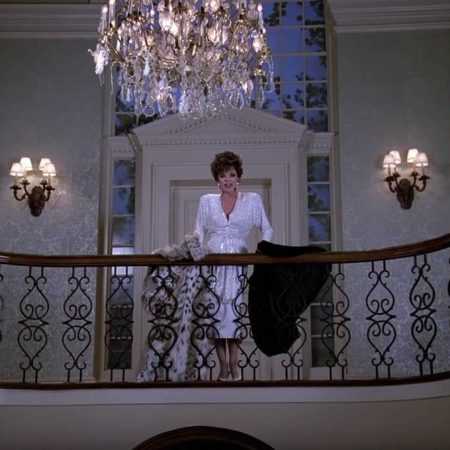 Alexis Carrington overlooking the foyer from the grand stairway where she's draped a fur coat over the handrail.