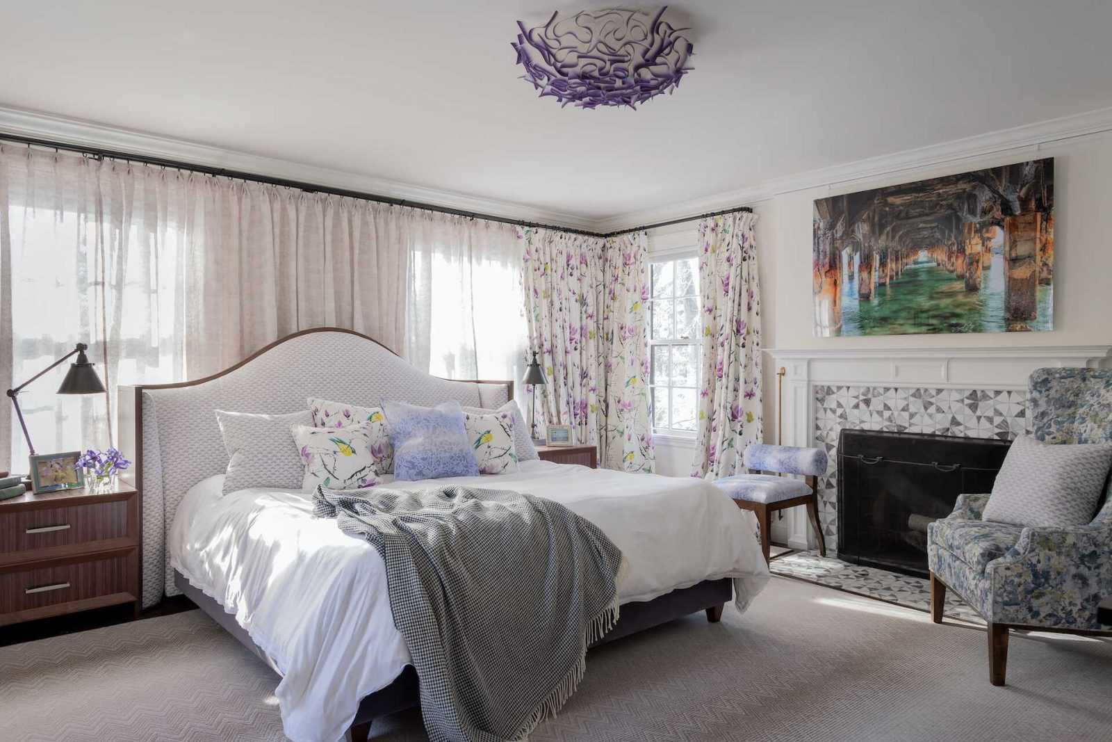 Master bedroom has playful purple hues, floral curtains, rosewood headboard and bedside tables, and a lilac marble fireplace.