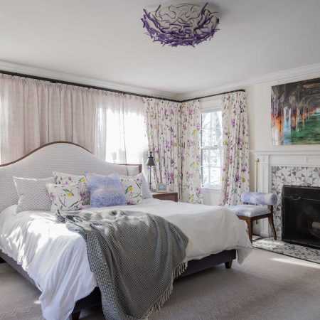 Master bedroom has playful purple hues, floral curtains, rosewood headboard and bedside tables, and a lilac marble fireplace.