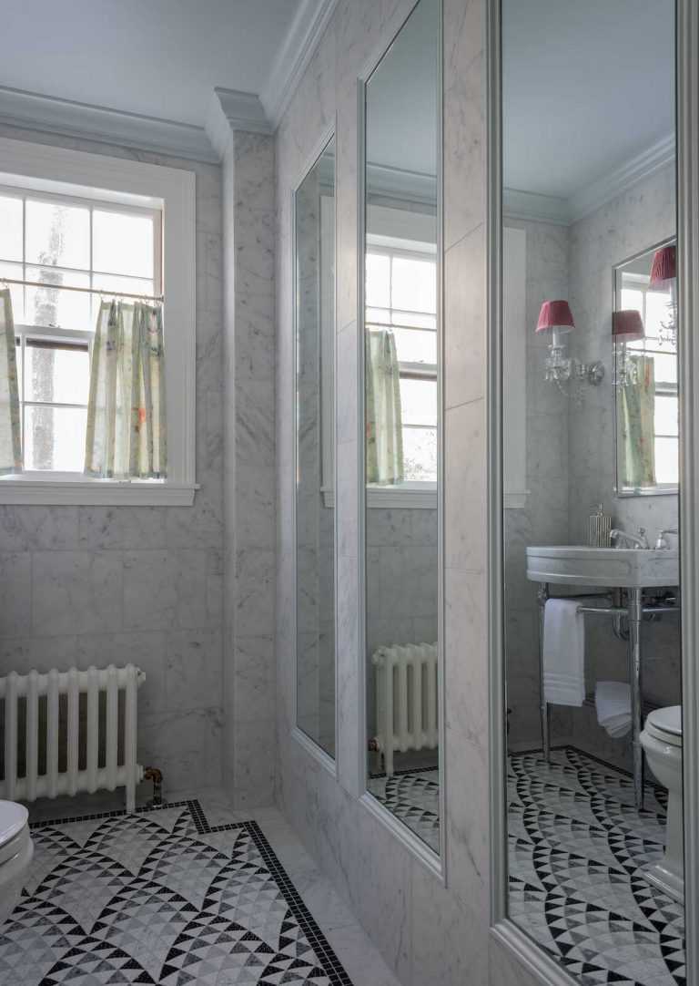 Mirrors inset in carrara marble tile walls reflect the carrara marble console sink and crystal sconces with red lampshades in the powder room.